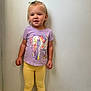 Everly is registered to the contest to win money with this photo: blonde_hair, bow, casual_clothing, child, cute, elephant_print, feet, floor, girl, happy, indoor, person, portrait, purple_tshirt, shoes, smile, standing, toddler, wall, yellow_leggings