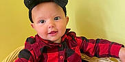 Paizley is registered to the contest to win money with this photo: baby, child, headband, bow, red_shirt, checkered, plaid, jeans, wicker_chair, indoor, smiling, cute, portrait, young_child, seated, person, clothing, furniture, face, happy