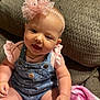 baby, child, infant, denim_overalls, pink_headband, flower_accessory, couch, blanket, indoors, smiling, sitting, cute, person, skin, face, hand, furniture, clothing, headwear, happy