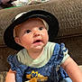 baby, child, hat, denim_dress, plush_toy, couch, blanket, indoors, cute, smiling, infant, person, clothing, face, sitting, young_child, headwear, toy, happy, portrait