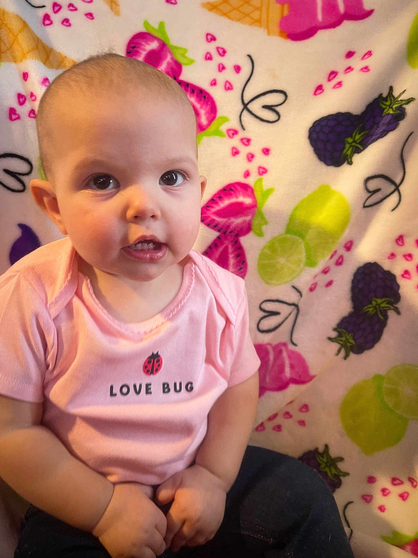 Paizley is registered to the contest to win money with this photo: baby, child, infant, pink_shirt, love_bug, fruit_pattern, blanket, strawberry, blackberry, lime, cute, portrait, sitting, indoor, face, hands, clothing, expression, young, person