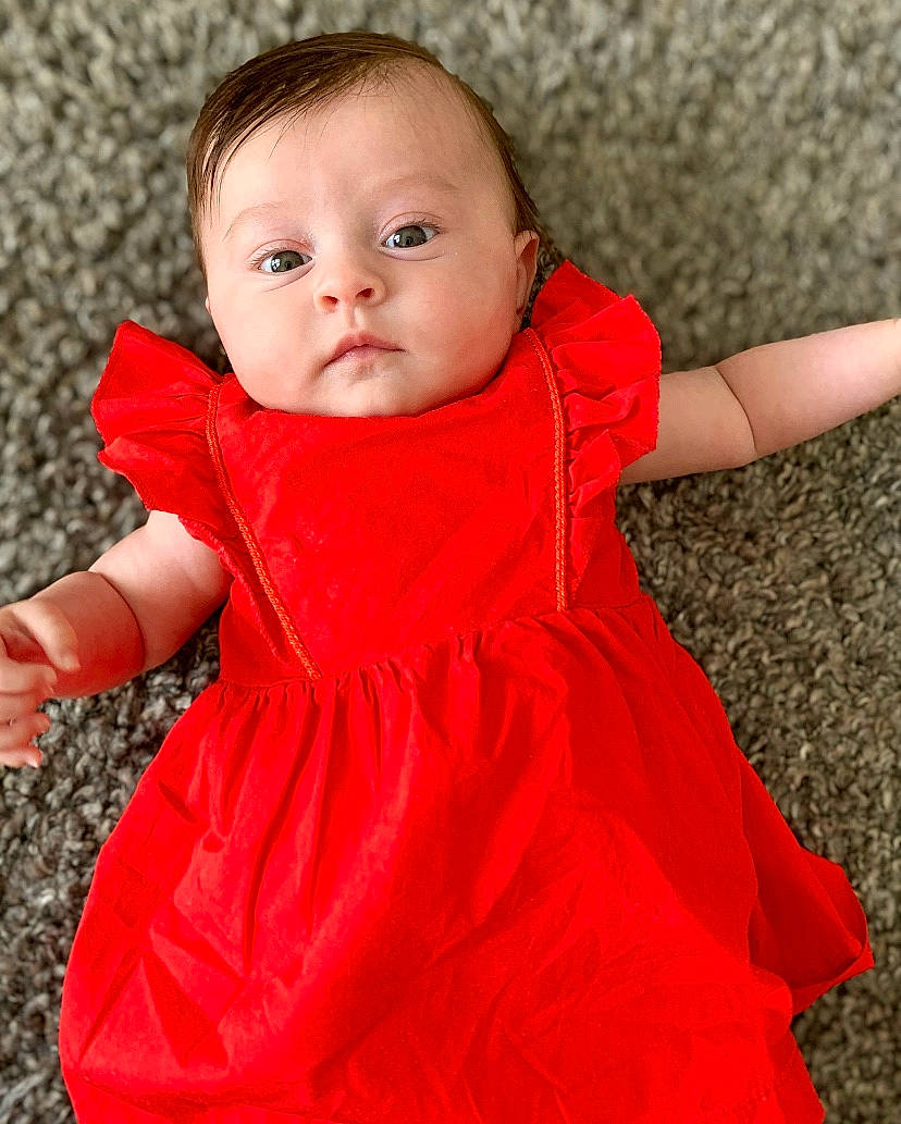 Danaë participe au concours pour gagner de l'argent avec cette photo : baby, baby_toddler_clothing, cheek, child, child_model, clothing, dress, outerwear, pattern, person, red, skin, sleeve, toddler