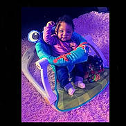 Journei is registered to the contest to win money with this photo: baby, child, infant, baby_seat, toy, purple_lighting, rug, clothing, smile, person, indoors, cute, raising_hand, sitting, face, happy, soft_texture, playtime, colorful, young