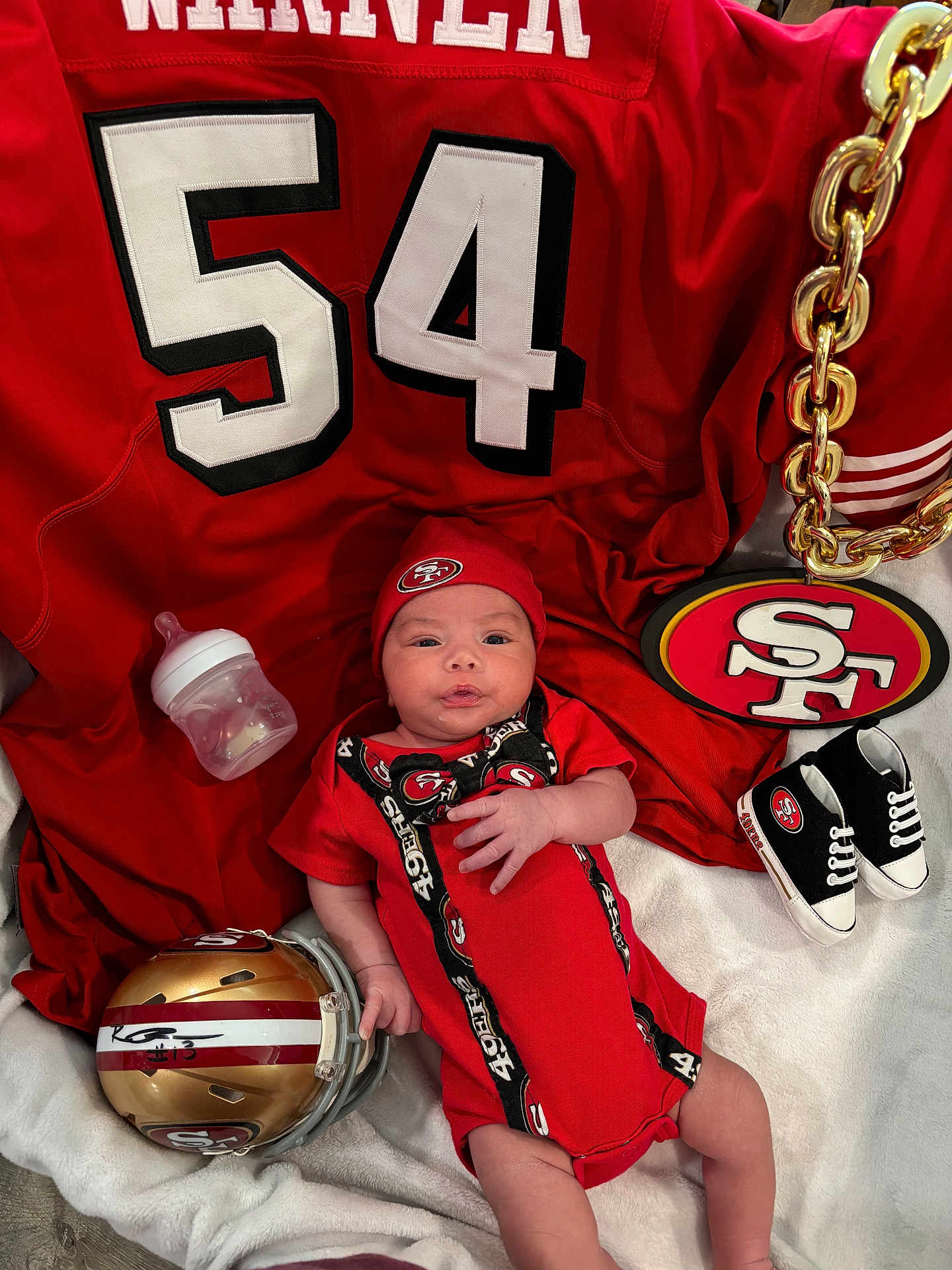 Memphis is registered to the contest to win money with this photo: baby, infant, red_clothing, football_helmet, bottle, blanket, baby_shoes, chain, sports_jersey, hat, logo, sports_fan, indoor, person, cute, laying_down, face, hand, footwear, accessory