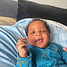 baby, infant, smiling, blue_outfit, blanket, hand, face, curly_hair, happy, indoors, bed, pillow, cute, child, person, portrait, cozy, soft, young, relaxed