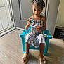 child, girl, braided_hair, blue_chair, dress, indoor, flooring, door, toy, footwear, sandals, natural_light, curious, painting, toenails, plastic_chair, young, person, portrait, home
