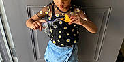 Nene is registered to the contest to win money with this photo: child, girl, toy, dinosaur_toy, bow, hair_bow, daisy_pattern, black_top, denim_skirt, sandals, indoor, wood_floor, door, standing, playing, casual_clothing, curly_hair, focused, childhood, imagination