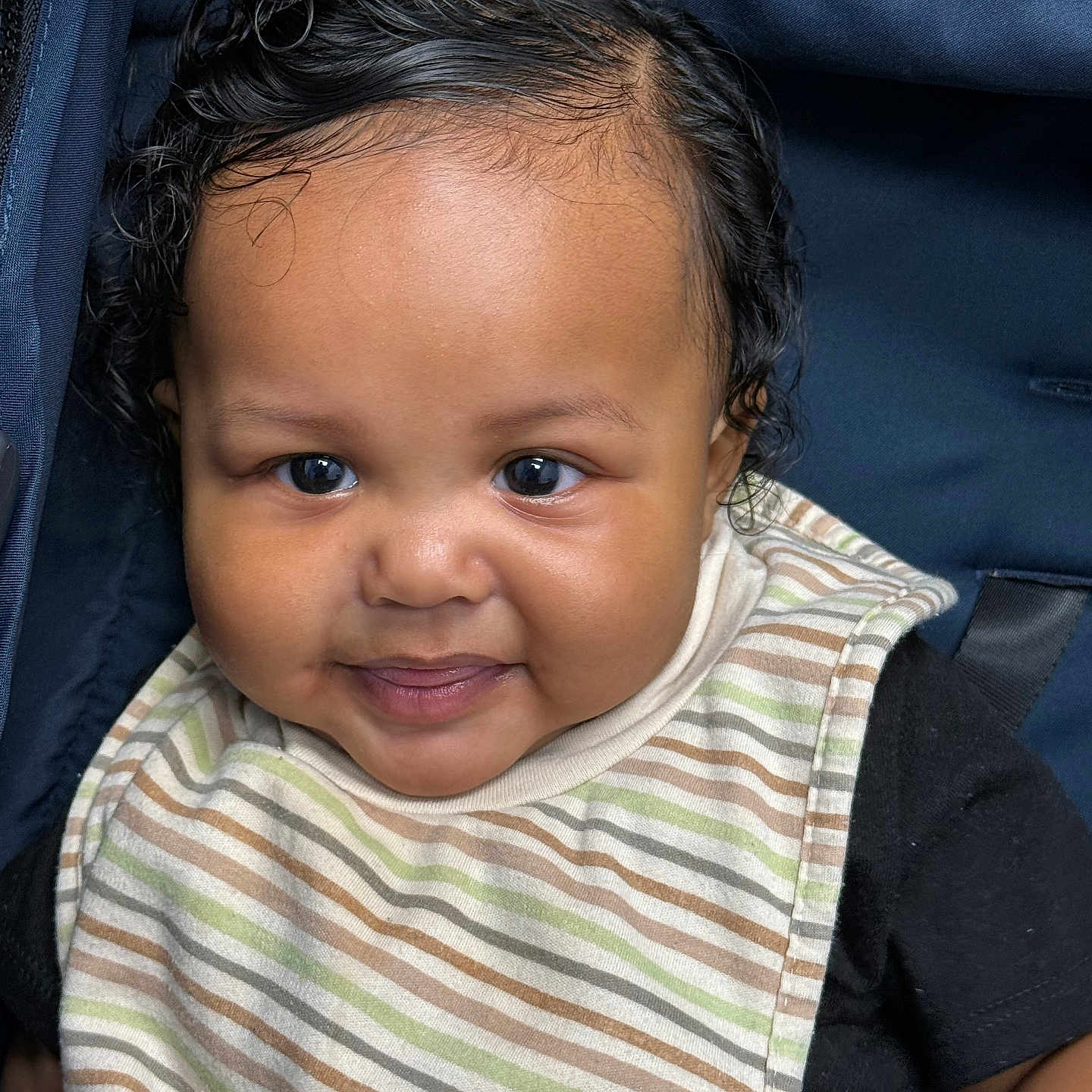 Kalen is registered to the contest to win money with this photo: baby, bib, black_shirt, car_seat, child, close_up, comfort, curly_hair, cute, expression, eyes, face, indoors, infant, portrait, seatbelt, smile, striped_bib, stroller, young_child