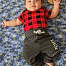 baby, infant, child, lying_down, red_shirt, checkered_pattern, grey_pants, barefoot, carpet, blue_carpet, textile, wooden_sign, four_months, smiling, cute, indoors, portrait, person, young_child, cozy