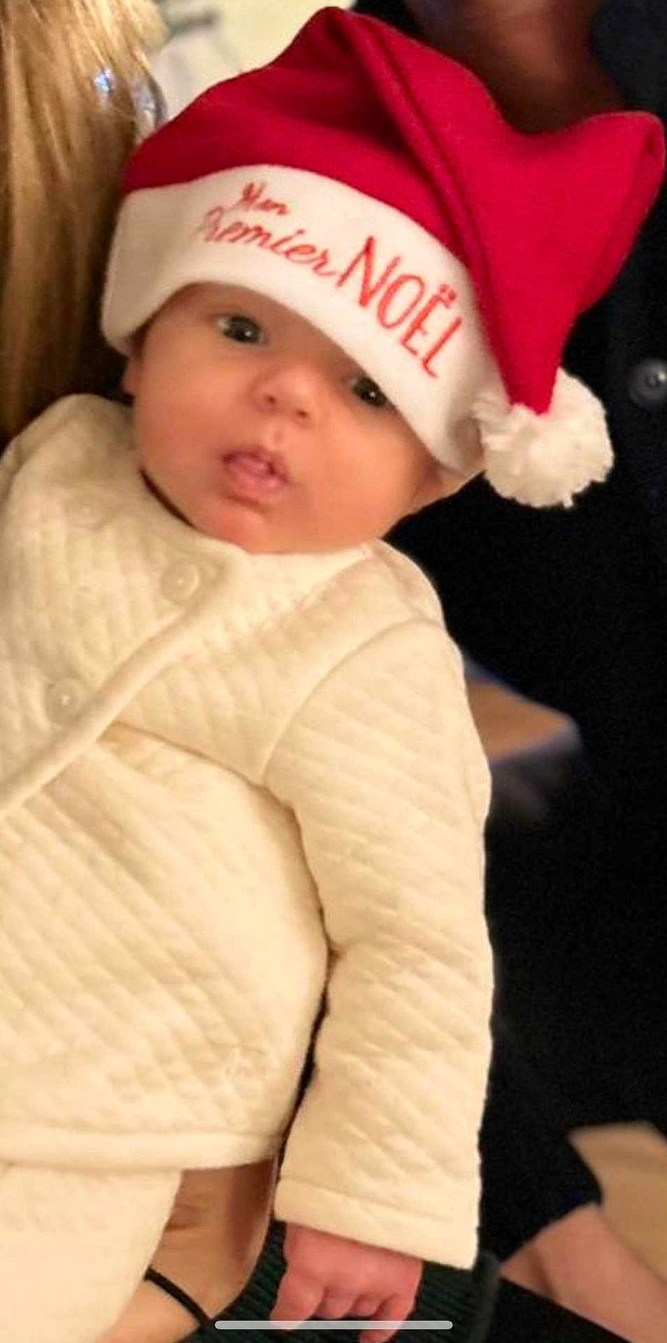 Leo a rejoint le concours — aidez-le/la à gagner de superbes lots ! baby, infant, child, santa_hat, christmas, holiday, festive, red_hat, white_hat, quilted_clothing, cream_clothing, person, face, cute, indoors, hand, adult, portrait, holiday_season, festive_clothing