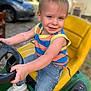 Ryder is registered to the contest to win money with this photo: toddler, child, smiling, outdoor, toy, tractor, yellow_seat, green_toy, steering_wheel, jeans, sneakers, casual_clothing, short_sleeves, blond_hair, playful, portrait, sunlight, background_blur, happy, fun