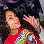 child, curly_hair, peace_sign, tongue_out, red_tshirt, spiderman, indoor, blanket, butterfly, bracelets, smiling, person, portrait, casual, bedroom, youth, happy, fun, cute, colorful