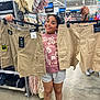 child, smiling, clothing_store, shorts, cargo_shorts, shopping, retail, happy, person, casual_clothing, store_shelves, price_tags, apparel, footwear, hanger, indoor, display, jeans, retail_environment, girl
