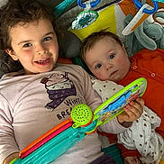 Léonie a rejoint le concours — aidez-le/la à gagner de superbes lots ! child, baby, smiling, toy, blanket, indoor, playtime, curly_hair, reading, colorful, happy, cute, infant, sibling, clothing, portrait, face, cuddly, playmat, relaxed