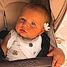baby, child, stroller, bugaboo, blue_eyes, flower, white_clothing, baby_yoda_print, hand, face, cute, portrait, infant, seatbelt, outdoor, sunlight, expression, closeup, skin, head