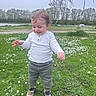 baby, casual_clothing, child, cute, daylight, flowers, grass, greenery, happy, nature, outdoor, park, person, shoes, sky, smile, standing, toddler, trees, young_child