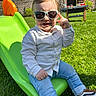 blue_jeans, casual_clothing, child, daytime, fun, garden, grass, green_slide, happy, lawn, outdoor, playground, pose, shoes, slide, smiling, sunglasses, sunny, toddler, white_shirt