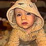 baby_clothing, bear_ears, blue_eyes, blurry_background, child, closeup, crawling, curious_expression, cute, face, fuzzy_outfit, hooded_onesie, indoor, infant, portrait, soft_lighting, soft_texture, toddler, warm_colors, young_child