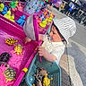 toddler, child, toy_turtles, plastic_toys, fishing_game, net, basket, pacifier, hat, striped_hat, outdoor, carnival, balloons, rubber_ducks, pink, water, play, curious, person, sunlight