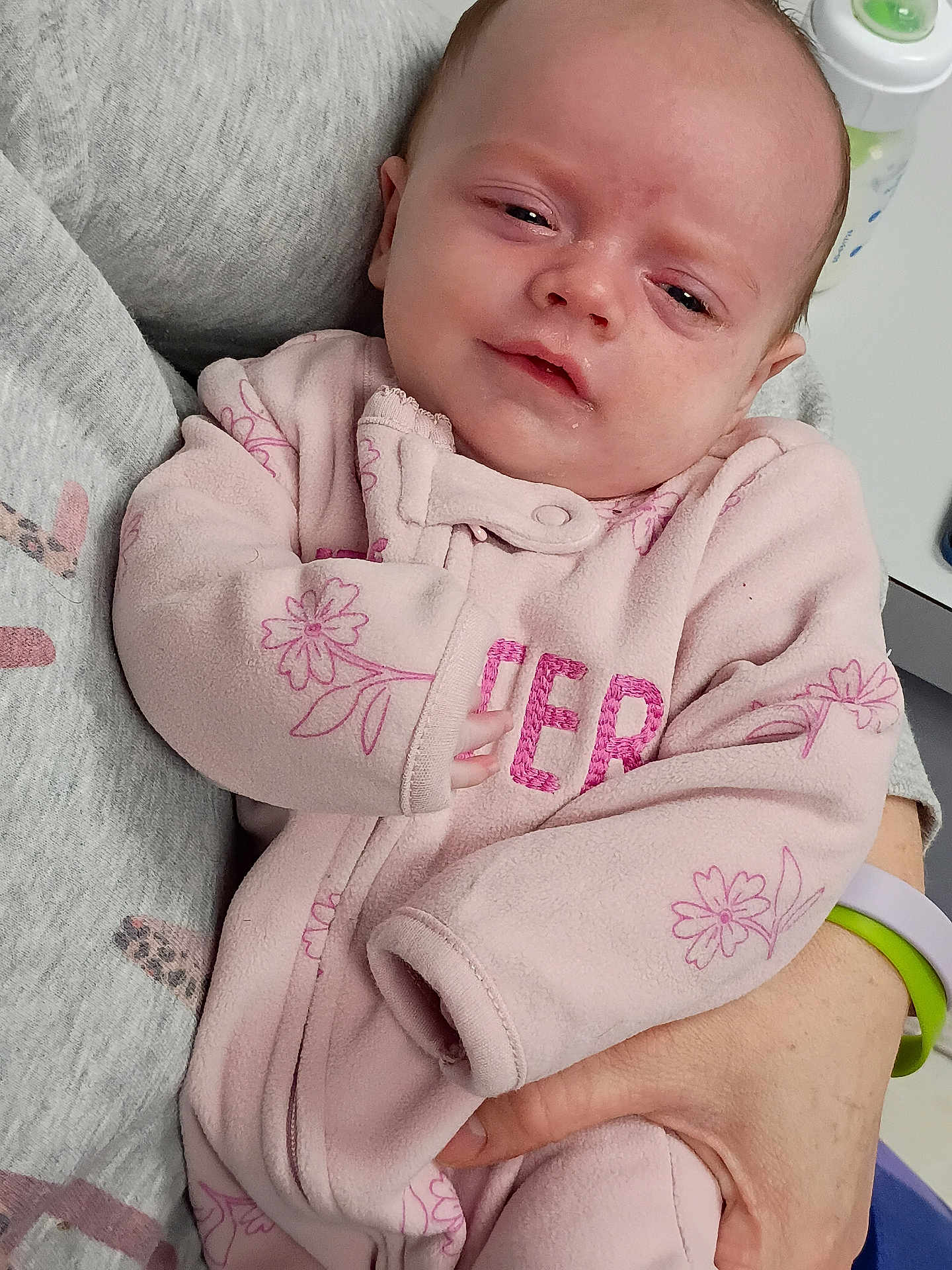 Brielle joined the competition — help win amazing prizes! baby, infant, child, pink_clothing, floral_pattern, onesie, person, holding, hand, adult, indoor, portrait, cute, young, sleepy, soft_texture, warm, closeup, face, expression