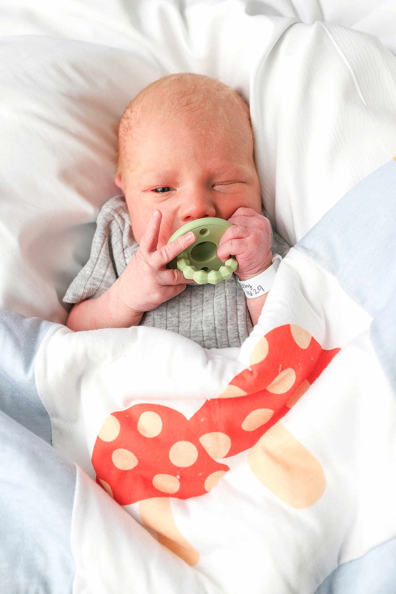 Flynn joined the competition — help win amazing prizes! newborn, baby, infant, blanket, teething_toy, hand, face, winking, wrapped, cozy, cute, sleepwear, bed, pale_skin, hospital_band, small_fingers, soft_light, portrait, indoors, resting