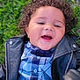 child, toddler, smiling, curly_hair, plaid_shirt, leather_jacket, grass, outdoor, happy, portrait, baby, casual_clothing, cute, young, person, face, nature, playful, joyful, lying_down
