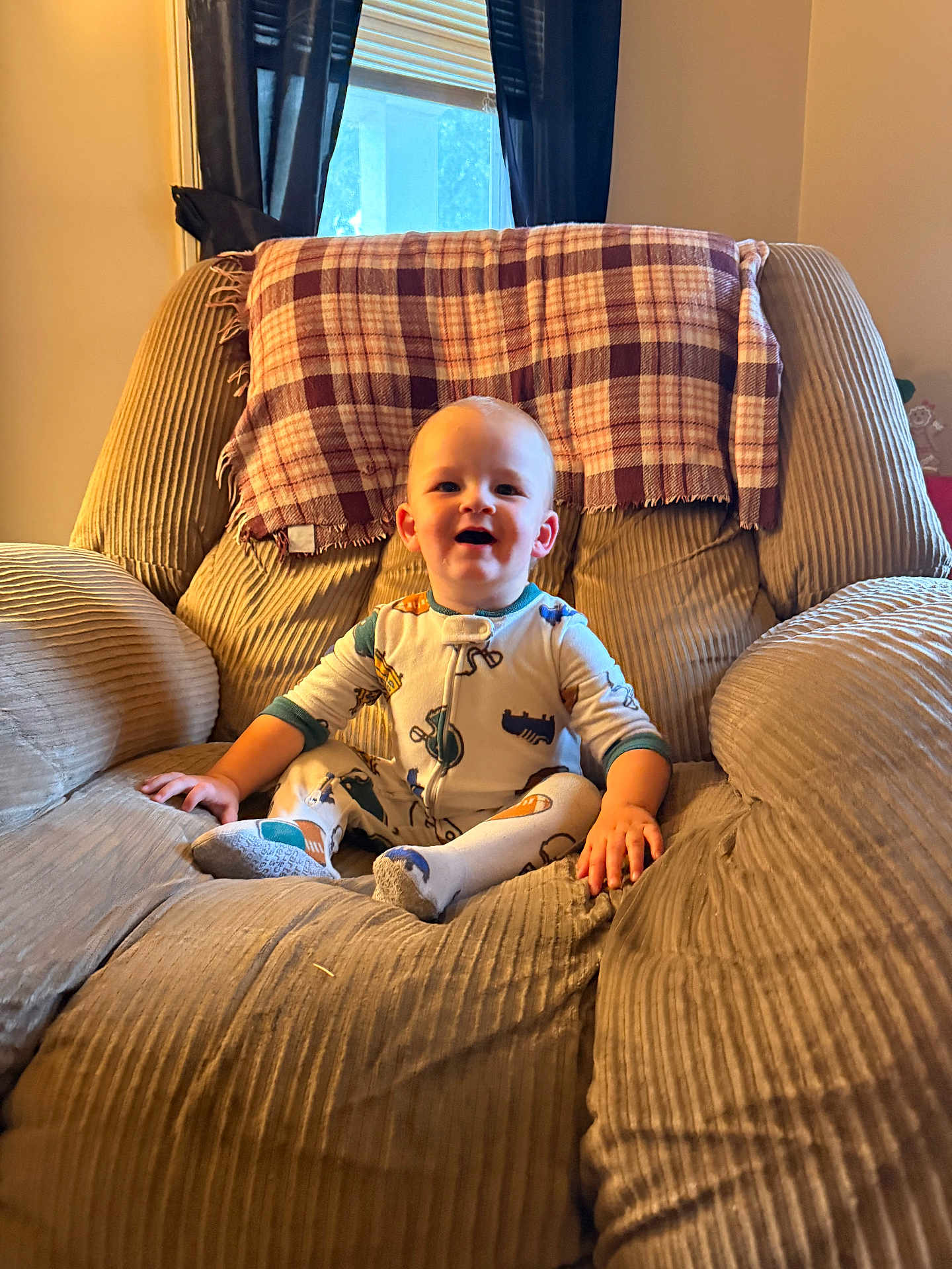 Hayson joined the competition — help win amazing prizes! baby, child, pajamas, armchair, plaid_blanket, window, curtains, indoor, smiling, seated, cozy, furniture, person, home, soft_lighting, cushion, happy, cute, toddler, room