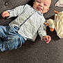 baby, smiling, tongue_out, striped_shirt, blue_jeans, couch, grey, plush_toy, infant, happy, child, indoor, casual_clothing, cute, playful, person, relaxed, sitting, young_child, home
