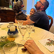 Nesta participe au concours pour gagner de l'argent avec cette photo : beard, bottle, candle, chair, child, collar, dining_room, dog, family, glass, glasses, hand, indoor, napkin, person, smile, table, tattoo, utensil, window