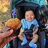 baby, smile, muffin, candle, stroller, blue_clothing, baby_socks, hand, outdoor, celebration, birthday, food, face, seatbelt, car_seat, person, happy, child, ground, grass
