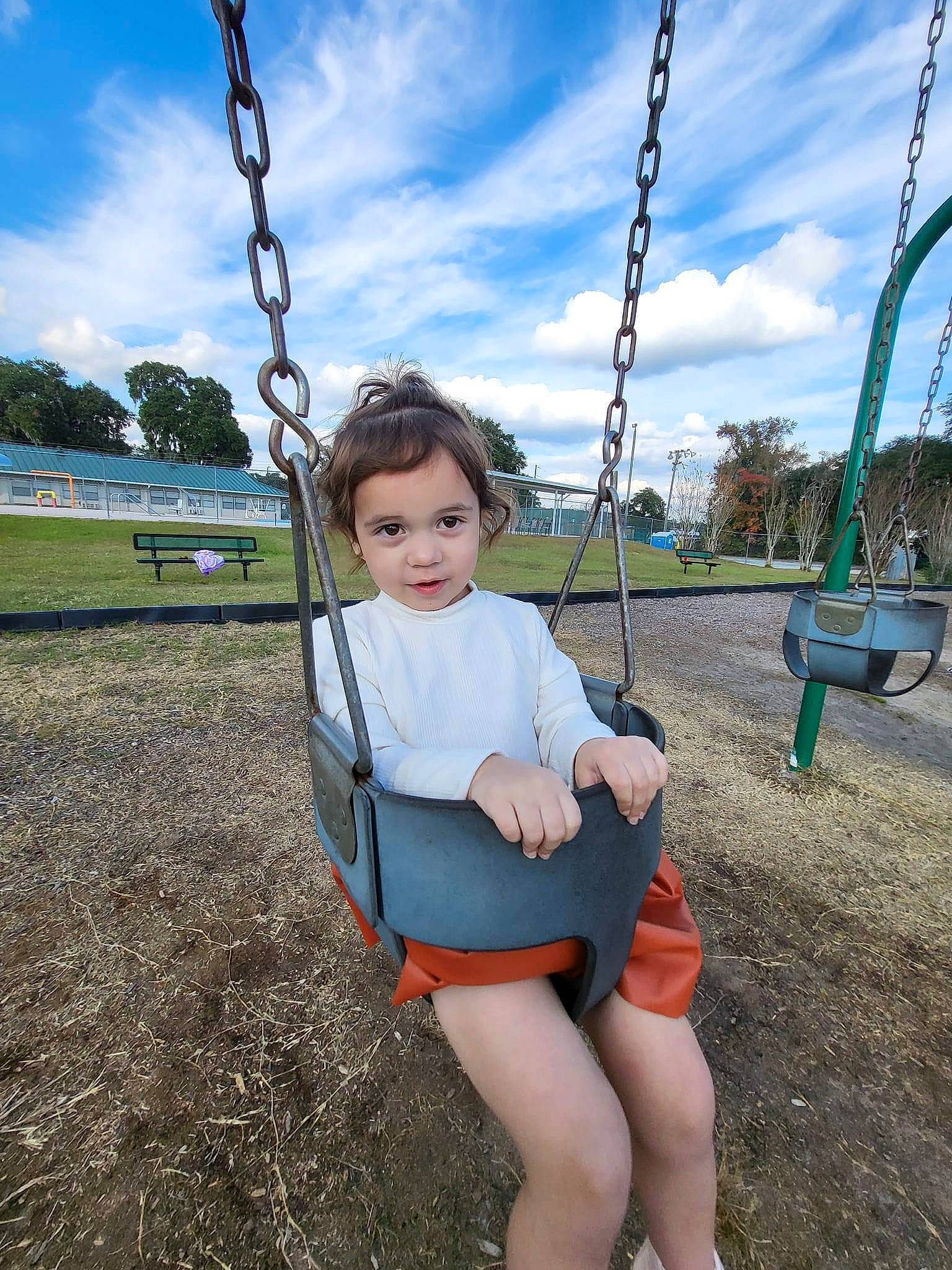 Tahlia is registered to the contest to win money with this photo: arm, blue, city, cloud, electric_blue, fun, grass, hand, happy, human_body, leisure, outdoor_play_equipment, person, plant, playground, recreation, sitting, sky, swing, toddler