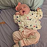 baby, infant, child, lying_down, bed, pillow, blanket, floral_clothing, pink_clothing, headband, bow, pacifier, socks, sleeping_area, indoors, portrait, cozy, surprised_expression, pastel_colors, photography