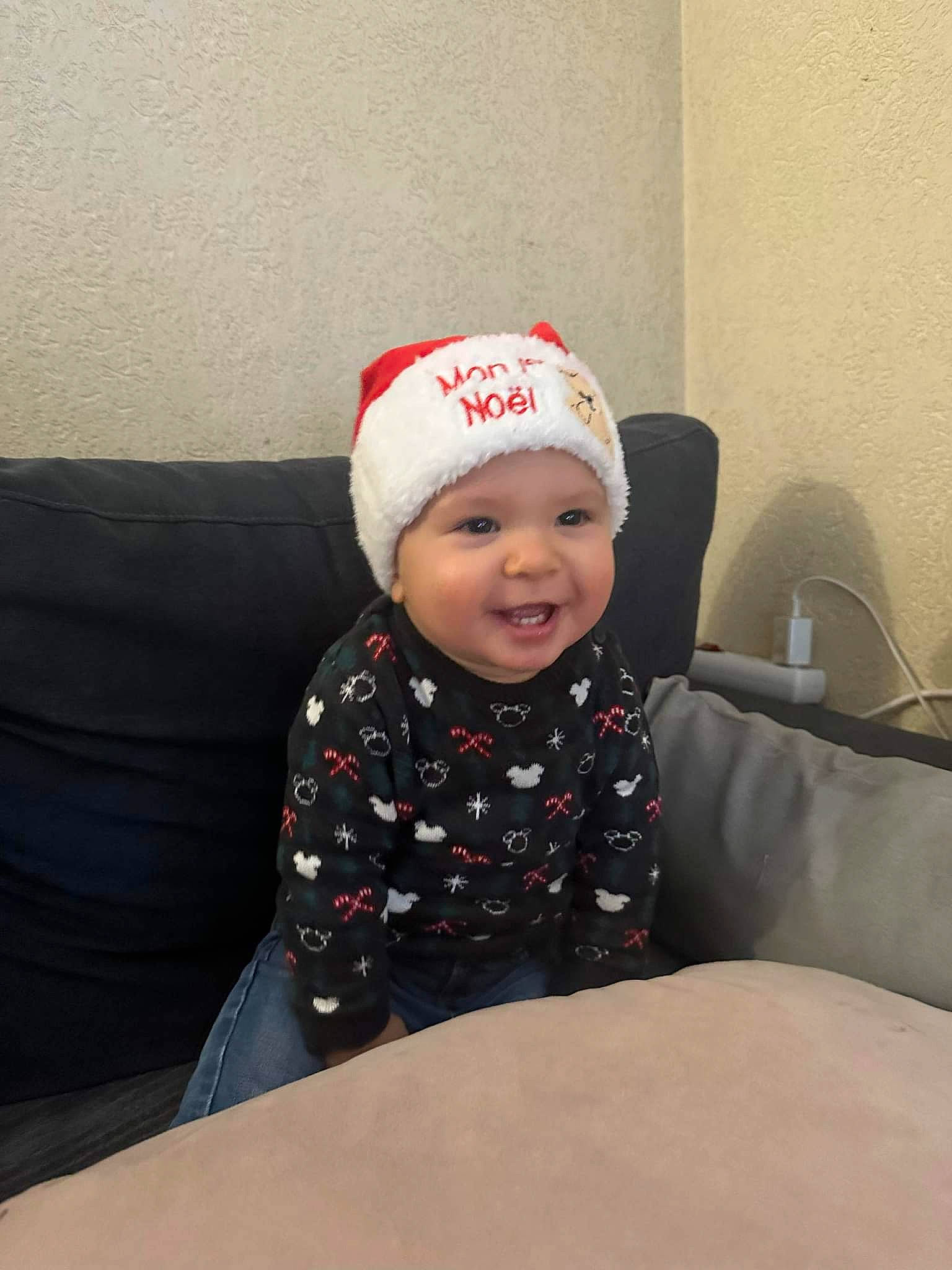 Mylann a rejoint le concours — aidez-le/la à gagner de superbes lots ! baby, baby_laughing, baby_toddler_clothing, beanie, cap, carmine, child, comfort, costume_hat, couch, fashion_accessory, flooring, fun, happy, headwear, holiday, person, room, sitting, sleeve