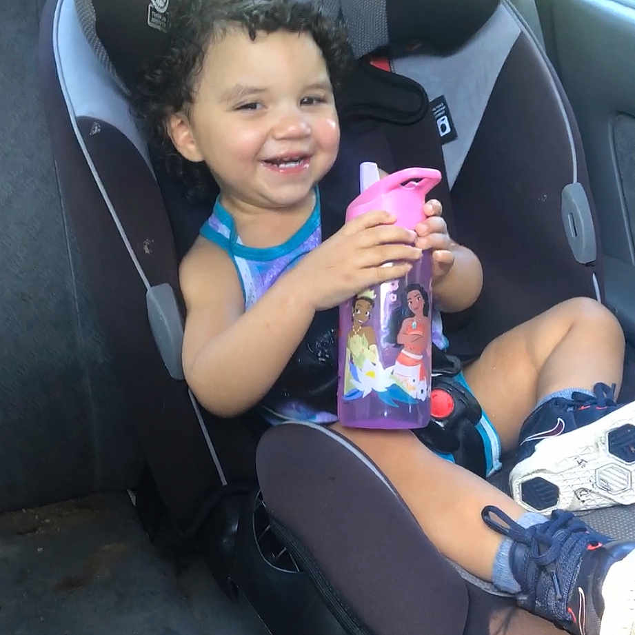 Zo-Rylah is registered to the contest to win money with this photo: car_interior, car_seat, casual_clothing, child, curly_hair, cute, daylight, drinking_bottle, happy, playful, portrait, safety_seat, seatbelt, sitting, smiling, sneakers, toddler, vehicle, water_bottle, young_child
