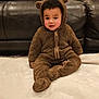 toddler, child, onesie, bear_costume, brown, blanket, couch, pillow, indoor, soft_texture, cute, young_child, face, sitting, cozy, home, furniture, portrait, warm, casual