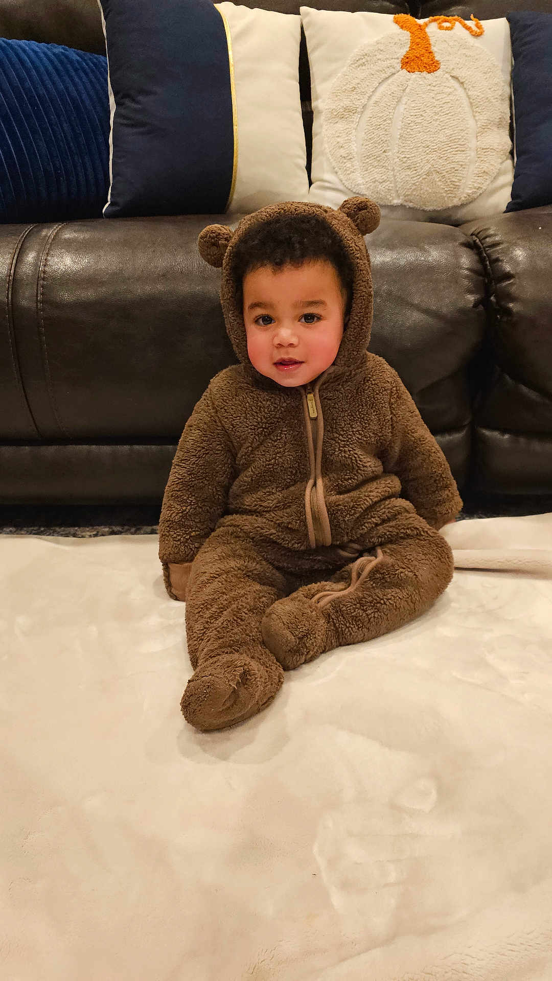Edson joined the competition — help win amazing prizes! toddler, child, onesie, bear_costume, brown, blanket, couch, pillow, indoor, soft_texture, cute, young_child, face, sitting, cozy, home, furniture, portrait, warm, casual