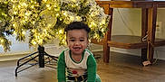 Edson is registered to the contest to win money with this photo: toddler, child, smiling, christmas_tree, holiday, pajamas, book, floor, indoors, decor, lights, wooden_floor, table, lamp, home, festive, joyful, cute, person, holiday_season