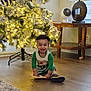 toddler, child, smiling, christmas_tree, holiday, pajamas, book, floor, indoors, decor, lights, wooden_floor, table, lamp, home, festive, joyful, cute, person, holiday_season