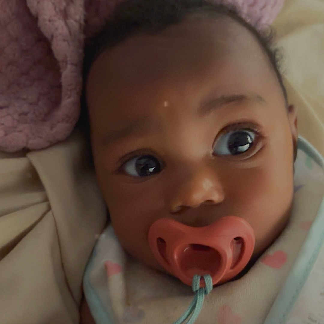 Bella is registered to the contest to win money with this photo: baby, blanket, child, closeup, comfort, cozy, curious, cute, face, heart_pattern, indoor, infant, newborn, pacifier, pink, portrait, resting, sleepwear, soft_texture, warm