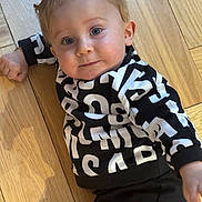 Sariel participe au concours pour gagner de l'argent avec cette photo : toddler, child, baby, floor, wooden_floor, sweater, black_and_white, pattern, lying_down, blue_eyes, face, portrait, curious, casual_clothing, indoor, person, young_child, smile, hand, hair