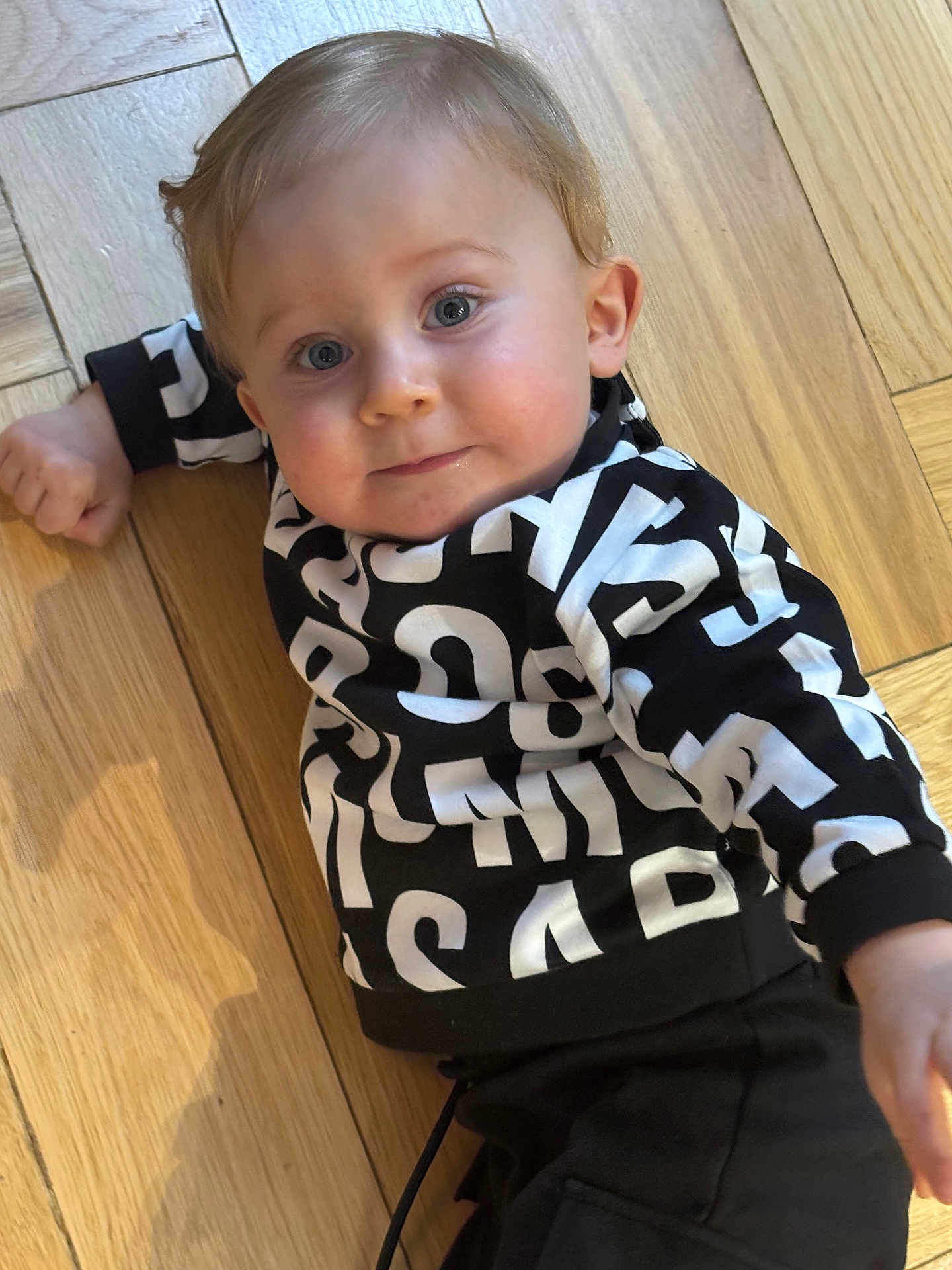 Sariel participe au concours pour gagner de l'argent avec cette photo : toddler, child, baby, floor, wooden_floor, sweater, black_and_white, pattern, lying_down, blue_eyes, face, portrait, curious, casual_clothing, indoor, person, young_child, smile, hand, hair