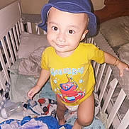 Richard joined the competition — help win amazing prizes! baby, baby_bottle, bedroom, blanket, child, clothing, crib, cute, face, furniture, happy, hat, indoor, person, playful, smile, standing, toddler, toy, yellow_shirt