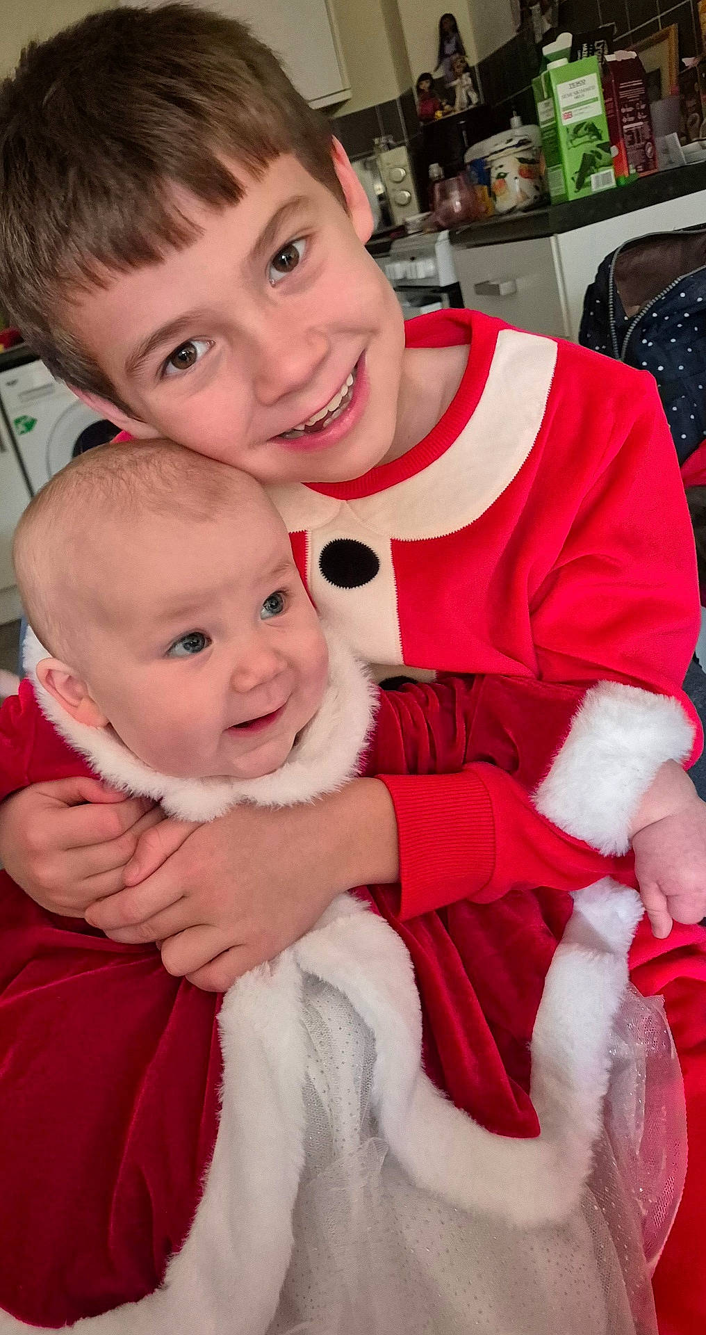 baby, celebration, child, cute, face, family, festive, happy, holiday_outfit, hugging, indoor, kitchen, person, portrait, red_clothing, siblings, smiling, toddler, white_trim, young