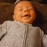 Stephen joined the competition — help win amazing prizes! baby, smiling, infant, onesie, clothing, face, happy, lying_down, child, cozy, soft, brown_background, cute, peaceful, indoor, portrait, young_child, baby_clothes, adorable, relaxed