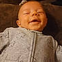baby, smiling, infant, onesie, clothing, face, happy, lying_down, child, cozy, soft, brown_background, cute, peaceful, indoor, portrait, young_child, baby_clothes, adorable, relaxed