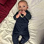 baby, infant, child, overalls, blue_clothing, black_socks, bed, quilted_bedspread, toy, braided_ring, lying_down, cute, curious, hand, face, blue_eyes, indoor, soft_lighting, blanket, sleepwear