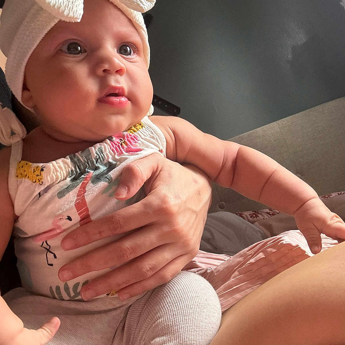 Azuriah is registered to the contest to win money with this photo: arm, baby, bed, blanket, bow, child, clothing, curious_expression, eyes, face, fingers, hand, headband, indoor, infant, mouth, person, sitting, skin, soft_light