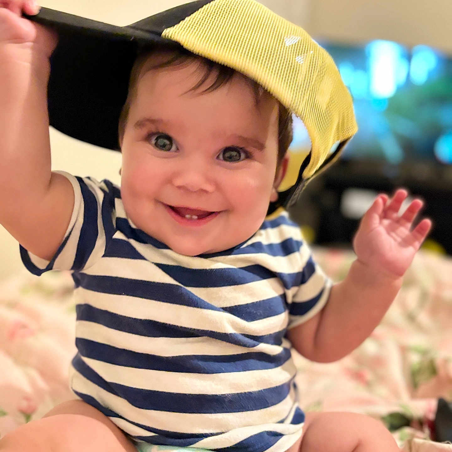 Toviyah is registered to the contest to win money with this photo: baby, child, smile, striped_shirt, cap, diaper, sitting, hand, face, happy, indoors, bedspread, playful, cute, young_child, person, portrait, infant, closeup, cheerful