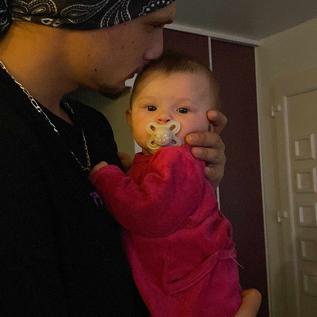 Lilo a rejoint le concours — aidez-le/la à gagner de superbes lots ! baby, man, pacifier, bandana, tattoo, indoor, holding, pink_clothing, person, portrait, face, warm_lighting, cozy, child, adult, love, family, affection, head, hand