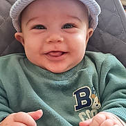 Giovanni participe au concours pour gagner de l'argent avec cette photo : baby, baby_seat, baby_toys, belltop, cap, child, clothing, cute, face, green_sweater, hands, happy, headwear, indoor, infant, person, portrait, seat, smile, young_child